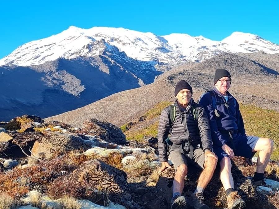 Two hikers resting on a rocky slope with a snow-covered mountain behind them